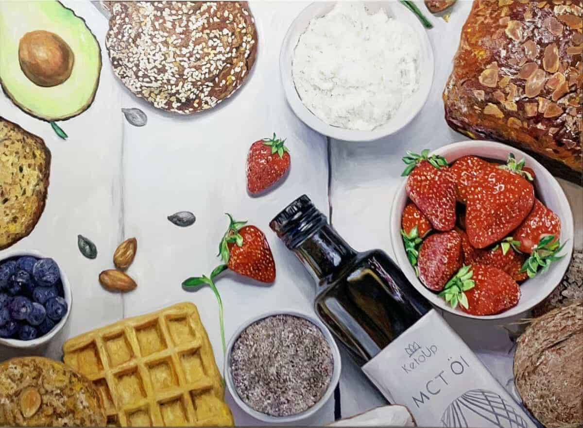 Brightly colored strawberries, blueberries, and avocado alongside baked bread, waffles, and pastries on a white wooden surface.