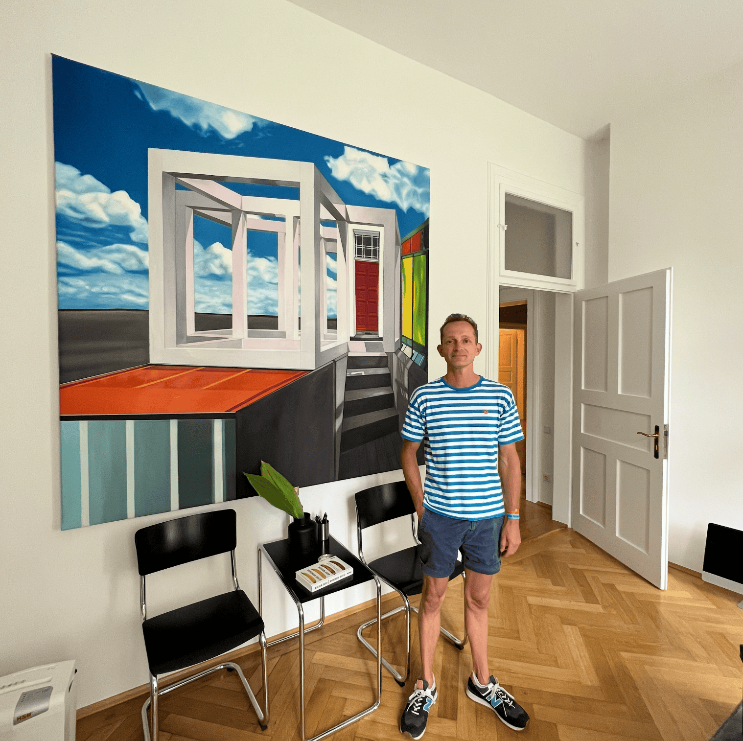 Portrait of Nikolaus Kriese standing in front of a large, colorful abstract painting in an art gallery or studio.