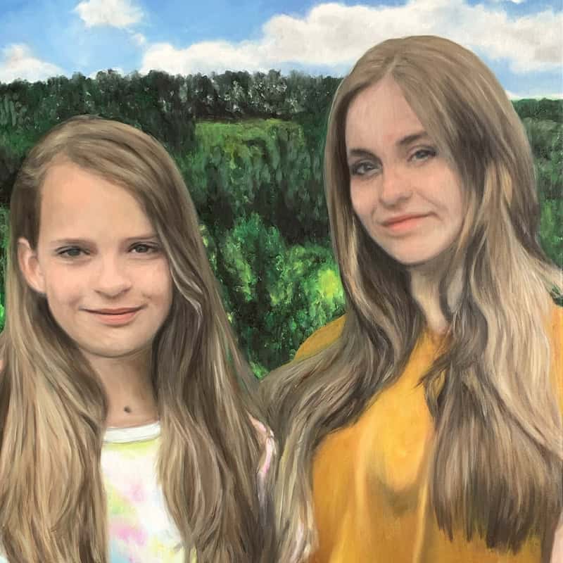 A portrait of two young women with long, flowing hair standing outdoors against a lush green landscape and blue sky.