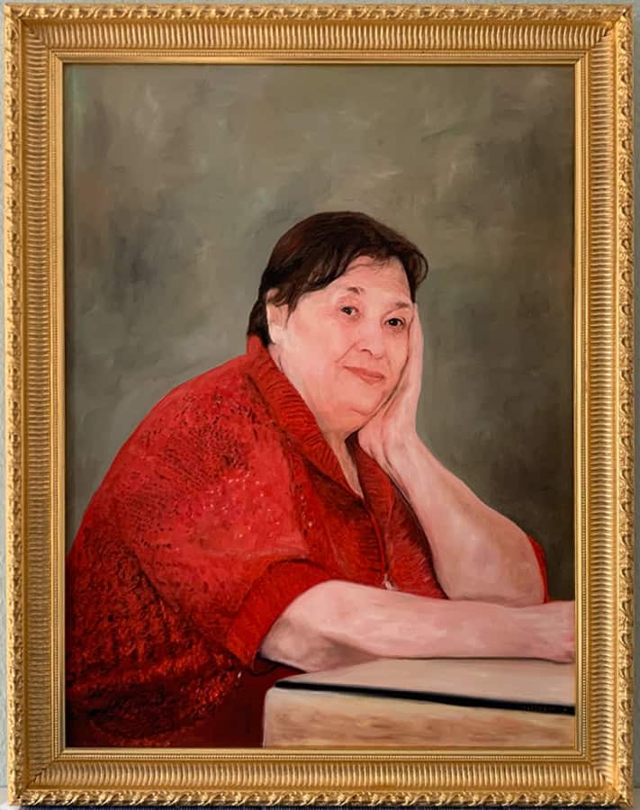 Portrait of an elderly woman in a red sweater, resting her head on her hand, with a contemplative expression, framed in an ornate gold frame.