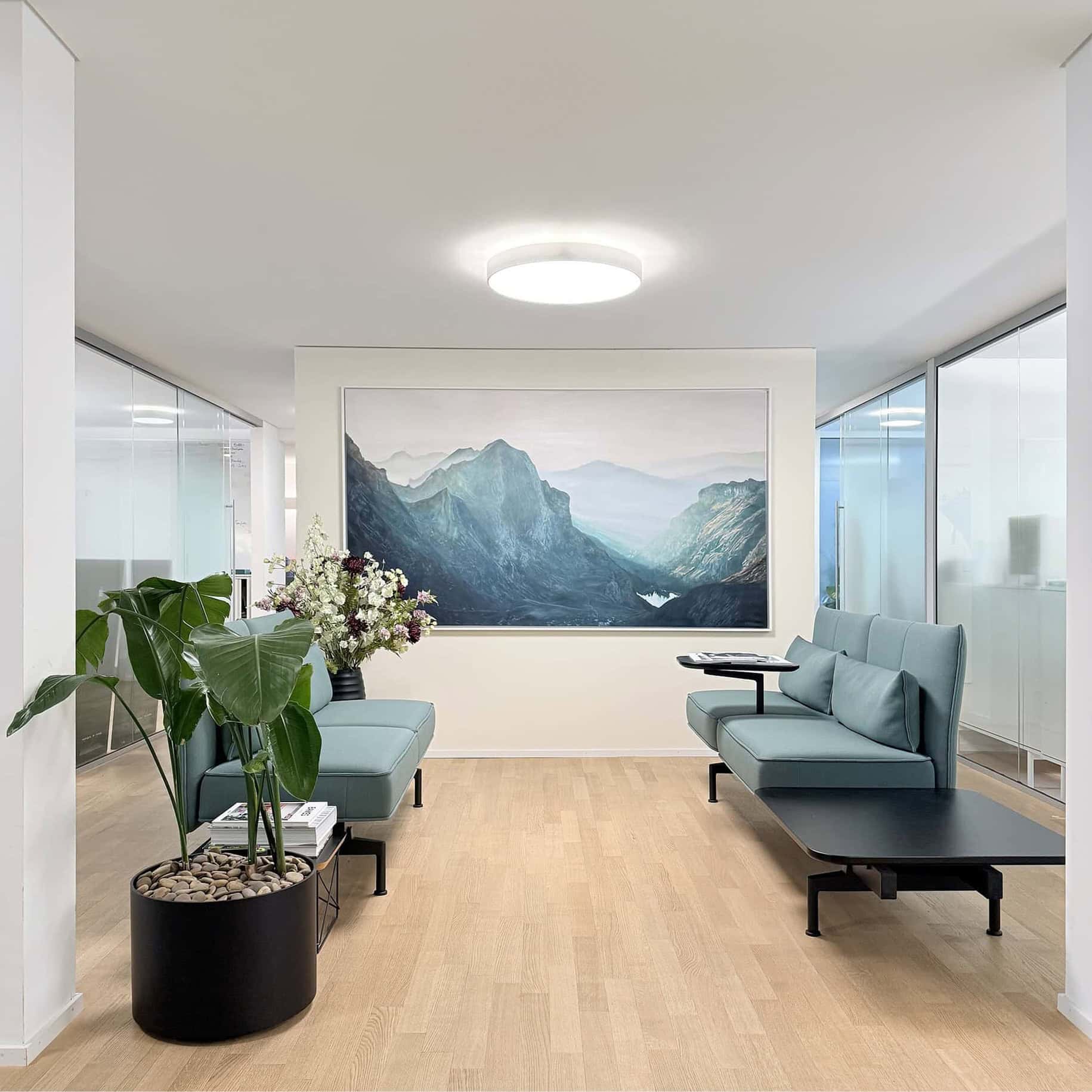 Modern waiting area with large mountain landscape painting, blue seating, and indoor plants, showcasing international art commission services.