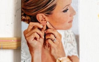 Portrait of a woman with styled hair, wearing jewelry, and adjusting her earrings.