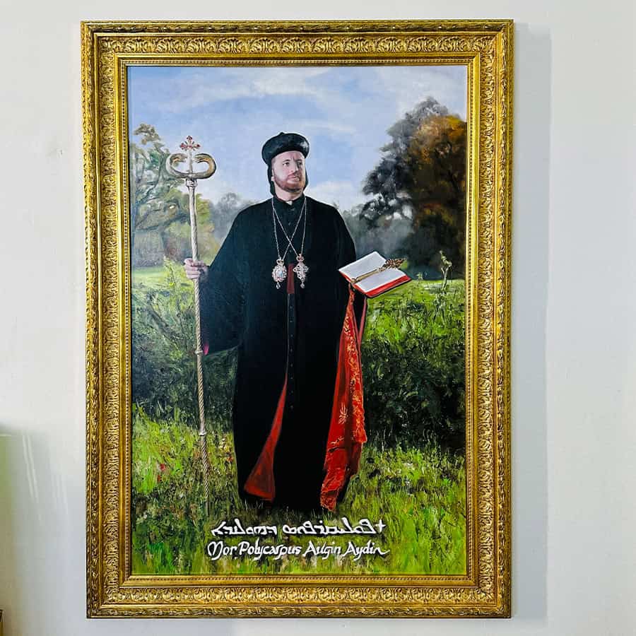 Portrait of a historical religious figure in traditional attire, holding a staff and an open book, set against a lush outdoor landscape background.
