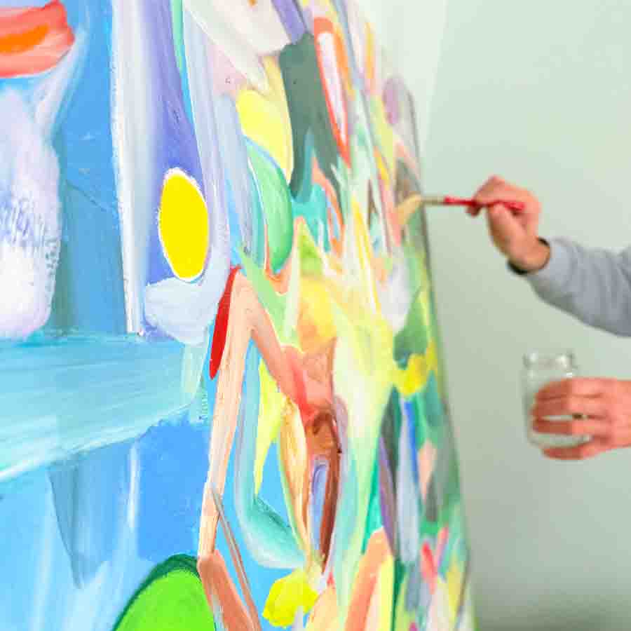 An artist painting a colorful abstract artwork on a large canvas, holding a brush in one hand and a glass of water in the other, showcasing his creative process and international art services.